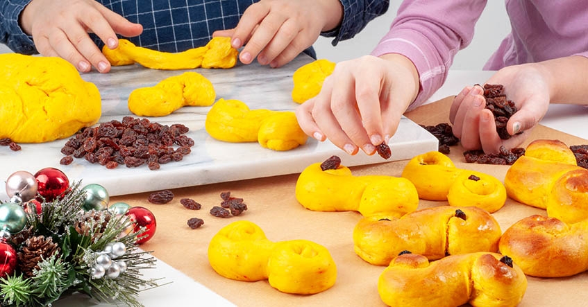 Deg för saffransbullar och färdiga lussekatter på ett bakbord med bakplåtspapper från Toppits