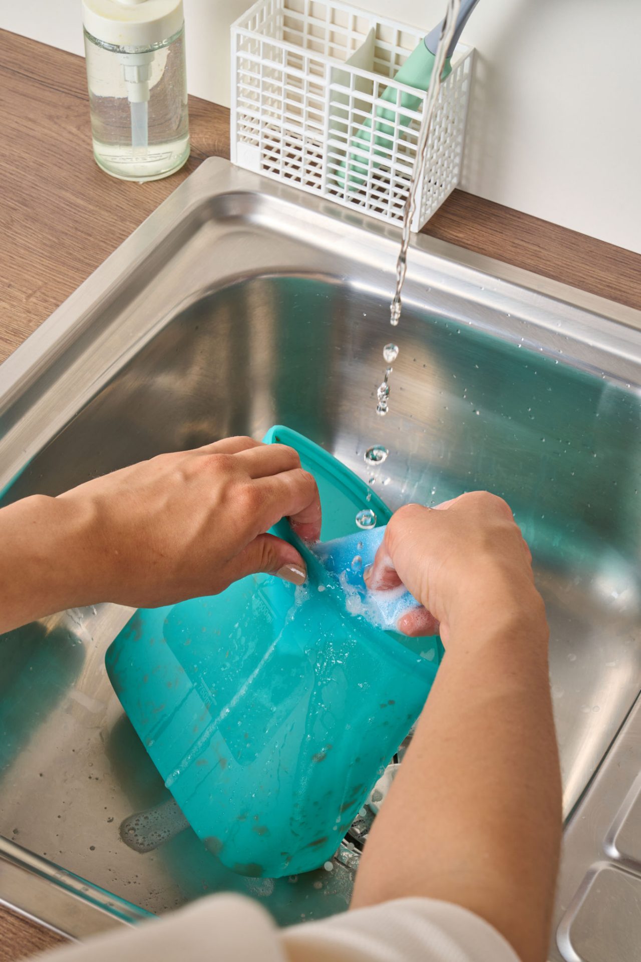 Person wäscht einen wiederverwendbaren Silikonbeutel unter fließendem Wasser in der Spüle.