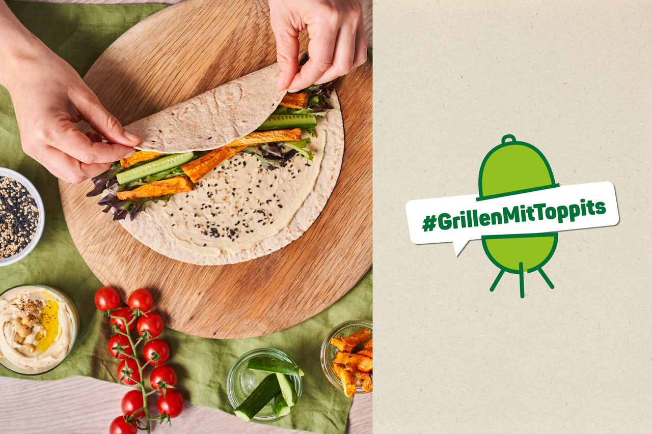 Hände rollen einen Wrap mit Grillgemüse und Hummus auf einem Holzbrett, daneben Tomaten, Gurken und Schälchen; rechts daneben ein #GrillenMitToppits Logo